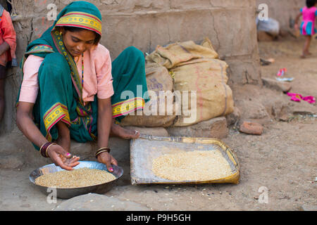 Une femme consulte ses céréales avant de faire de la farine devant son domicile à Sendhwa, Inde. Banque D'Images