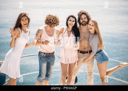 Les jeunes riches amis, habillés en vêtements d'été en bateau pour s'amuser, boire du vin, sur un arc de yacht de luxe. Banque D'Images