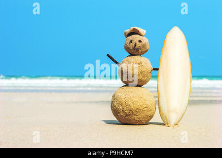 Sandman joyeuse surfer avec une planche de surf sur le sable contre l'eau de mer turquoise. Noël et nouvel an concept sur une plage tropicale. Des couleurs vives. concept o Banque D'Images