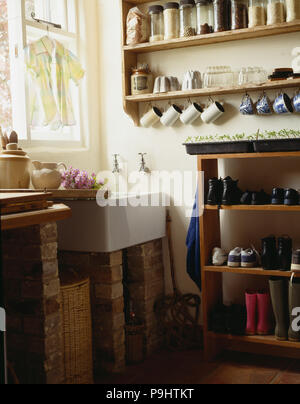 Pots de stockage sur des étagères au-dessus du lavabo blanc rustique en buanderie avec chaussures stockés sur des étagères en bois Banque D'Images