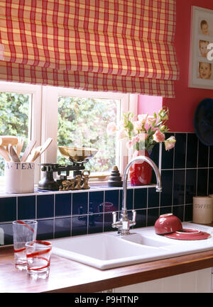Vu rouge aveugles sur fenêtre au-dessus de lavabo dans années 90 cuisine avec carrelage bleu Banque D'Images