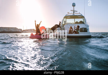 Groupe d'amis profitant d'une journée d'été sur un jouet gonflable et yacht. Les jeunes d'avoir du plaisir. L'homme de la plongée en mer avec des amis encouragements de location