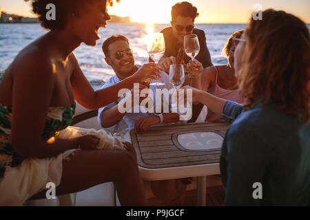 Groupe d'happy friends cheering avec vin et bières au parti en bateau. Diversité des hommes et des femmes ayant des boissons au coucher du soleil à partie. Banque D'Images