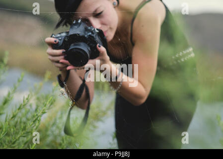 Belle jeune femme photographe portant des vêtements noirs de prendre des photos macro de la nature et des insectes à l'extérieur. Tiger araignée dans sa toile d'araignée étant phot Banque D'Images