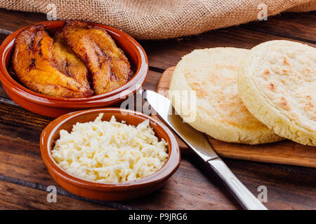 Petit-déjeuner vénézuelien, Arepas sur planche de bois et à côté un récipient avec du fromage et un autre avec le plantain frit à remplir Banque D'Images