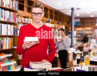 Jeune homme élégant cavalier rouge dans le choix de livres en librairie Banque D'Images