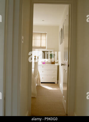 Voir par porte ouverte de petite chambre blanche avec une moquette crème et une commode laqué blanc Banque D'Images