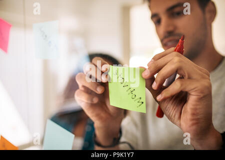 L'homme écrit sur les notes avec feutre et collage sur verre conseil en bureau. Entrepreneurs de discuter affaires des idées et des plans avec les notes Banque D'Images