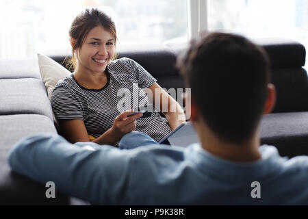 Young hispanic couple portant sur la table à la maison, à l'aide d'un tablet PC et carte de crédit pour l'achat en ligne. Le petit ami est de donner un massage aux pieds de Banque D'Images