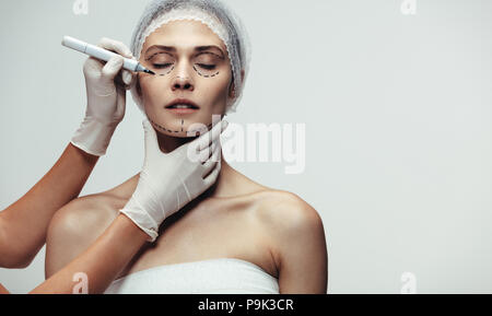 Les mains du médecin de faire les pointillés sur visage féminin pour l'ascenseur de visage cosmétique contre fond gris. Surgeon drawing dotted lines on patient visage avant su Banque D'Images