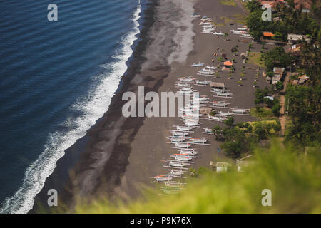 Plage de sable noir avec beaucoup de bateaux traditionnels balinais, vue à partir de la falaise à Candidasa Banque D'Images