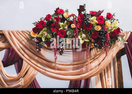 Cérémonie de mariage style Boho, décorées avec des roses rouges, jaunes, orchidées et de raisin pourpre et le tissu beige Banque D'Images