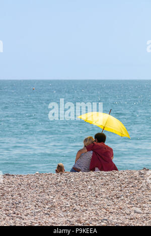 Worthing, Royaume-Uni ; 14 juillet 2018 ; Vue arrière du couple sur la plage, sous un parasol jaune au cours de fortes chaleurs en été Banque D'Images