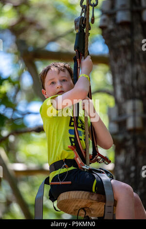 Portrait d'un beau garçon sur une corde entre les arbres du parc. Activités d'été pour enfants. Banque D'Images