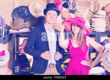 Heureux que la femme et l'homme d'essayer sur la mode chapeaux dans le shopping mall Banque D'Images