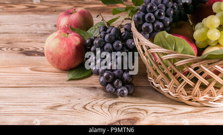 Pommes rouges bien mûrs avec des feuilles, le raisin noir et blanc dans un panier. Chasse d'automne. Close-up. Banque D'Images