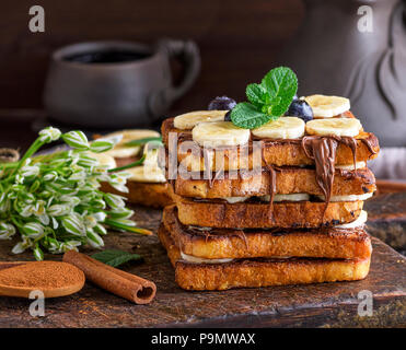 Poêlée de morceaux de pain blanc dans un œuf avec le lait et enduit de chocolat, pain doré avec une banane sur une planche en bois brun Banque D'Images