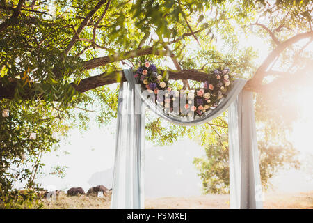 Coucher du soleil de la cérémonie du mariage, arche décorée de tissu gris pendaison le grand arbre et l'arrangement fleurs rose Banque D'Images