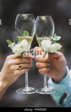 L'homme et la femme hands holding two champagne glasses décorées de fleurs pour la cérémonie du mariage Banque D'Images