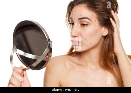 Jeune femme avec la peau problématique et sans maquillage à son soi dans le miroir sur un fond blanc Banque D'Images