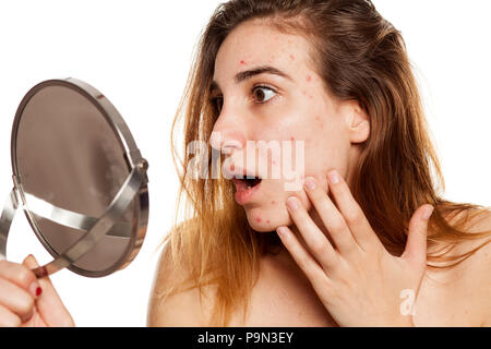 Jeune femme choqué avec la peau problématique et sans maquillage à son soi dans le miroir sur un fond blanc Banque D'Images