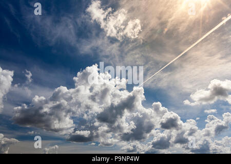 D'énormes cumulus et un long trail blanc d'un avion dans un ciel lumineux bleu, plusieurs rayons de soleil dans la photo d'illuminer le paysage Banque D'Images