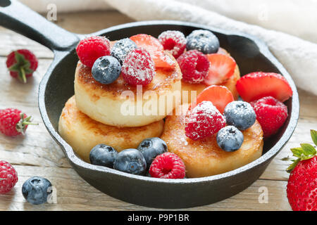 Crêpes au fromage cottage, syrniki, beignets de pâte avec les baies fraîches (framboise, fraise, myrtille, mûre) et de sucre en poudre dans une fonte pa Banque D'Images