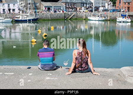 Un jeune homme et femme assis sur le quai au port de Padstow Cornwall UK de déguster une boisson sur une chaude journée d'été Banque D'Images