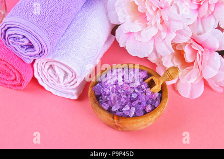 Spa sur un fond pastel rose. Serviettes, pierres, aromamaslo, bain de sel pourpre et des fleurs roses Banque D'Images