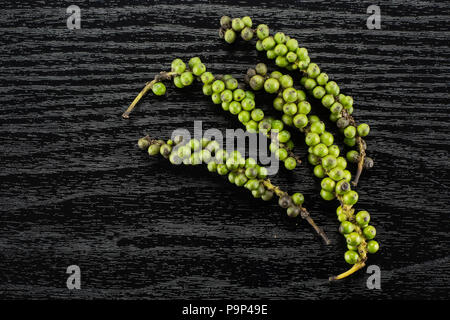 Drupes vertes de poivre noir frais flatlay sur fond de bois noir quatre grappes Banque D'Images