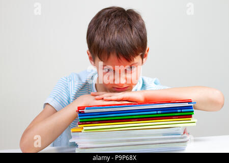 Écolier en colère sitting at desk with pile de livres et cahiers scolaires Banque D'Images