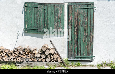 Gros plan d'une façade en bois rustique avec des volets verts et porte et bois de chauffage Banque D'Images