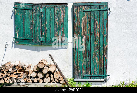 Gros plan d'une façade en bois rustique avec des volets verts et porte et bois de chauffage Banque D'Images