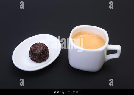 White tasse de café espresso classique et pralines sur fond noir. Banque D'Images