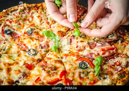 Woman's hands décorez pizza italienne avec des feuilles de basilic frais Banque D'Images