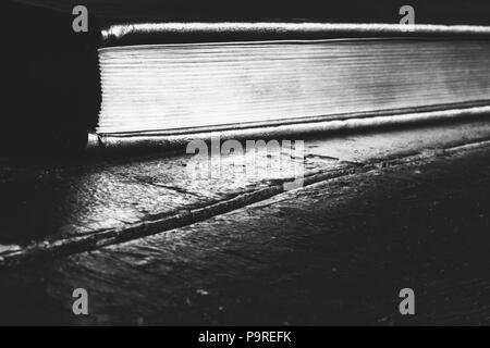 Un livre fermé avec une pointe d'or sur une vieille table en bois noir avec copie espace photo en noir et blanc. Banque D'Images