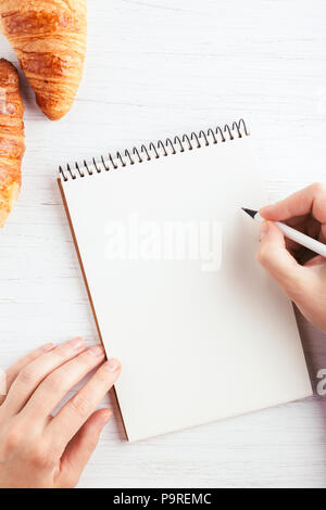 Woman's hand writing in notebook sur table en bois blanc. Lieu de travail et de planification, conception, temps matin vue du dessus. Banque D'Images