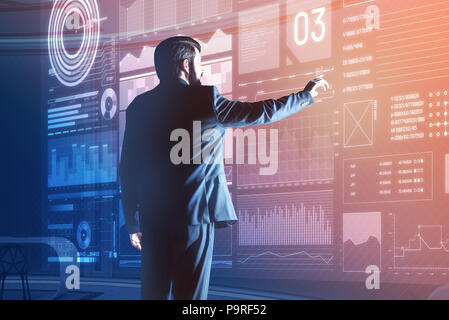 Travailler avec l'appareil futuriste. Développeur de logiciels professionnels intelligente portant un costume noir et à la calme tout en touchant l'écran de Banque D'Images