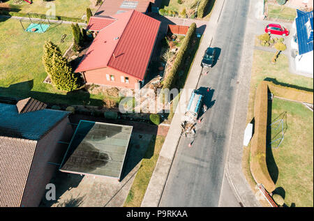 Vue aérienne d'une simple maison individuelle sur une route asphaltée gray village road, sur lequel un ouvrier n'effectue des travaux de maintenance, faites avec drone Banque D'Images