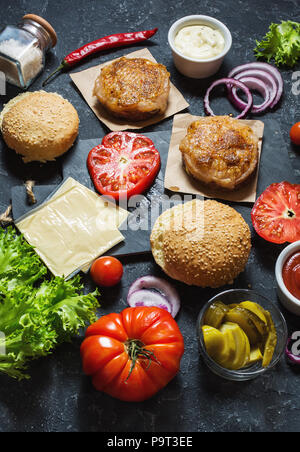 Ingrédients pour la cuisson burger. Patty poulet grillé, petits pains, l'oignon, les tomates, cornichons, sauce fromage sur fond noir Banque D'Images