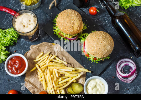 Hamburgers maison au boeuf et pommes de terre sautées et un verre de bière brune froide sur table en pierre. Vue d'en haut Banque D'Images