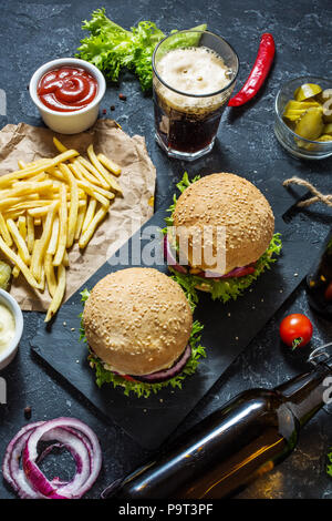 Hamburgers maison au boeuf et pommes de terre sautées et un verre de bière brune froide sur table en pierre. Banque D'Images