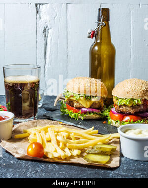 Hamburgers maison au boeuf et pommes de terre sautées et un verre de bière brune froide sur table en pierre. Banque D'Images