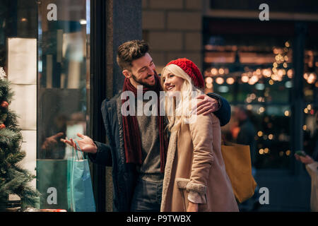 Vue latérale d'un couple à la recherche à travers la vitrine d'un magasin tout en achats de noël ensemble. Banque D'Images