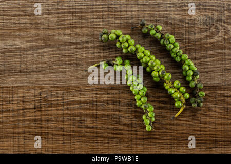 Drupes vertes de poivre noir frais flatlay sur fond brun bois trois grappes Banque D'Images