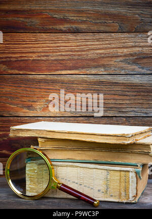 Une pile de vieux livres et la loupe sur fond de bois. Le concept de la recherche, l'étude de l'espace pour le texte. Banque D'Images