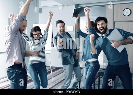 Nous l'avons fait. Heureux smiling jeunes collègues debout dans l'office et célébrer ensemble réussie du projet Banque D'Images