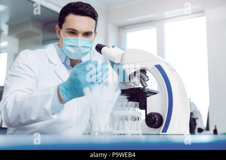 La recherche moderne. Smart professionnel male scientist en uniforme à la recherche et le tube à essai tout en travaillant dans le laboratoire Banque D'Images