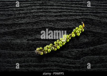 Drupes vertes de poivre noir frais flatlay sur fond d'un tas de bois noir Banque D'Images