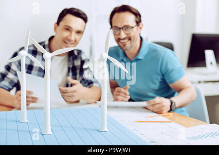 Des collègues. positif Happy friendly cheerful ingénieurs assis dans leur bureau avec un modèle d'un générateur moulin à vent sur la table Banque D'Images